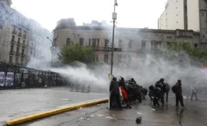 Los manifestantes se cubren del agua de un camión hidrante y de los gases durante los incidentes en la plaza del Congreso.